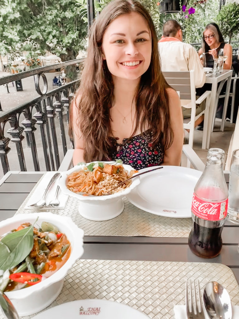 A picture of Grace a few weeks after her first seizure. She is sitting on a balcony with a plate of food and smiling at the camera.