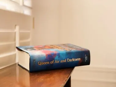 A hardback copy of Queen of Air and Darkness sitting on a table edge, spine facing the camera.